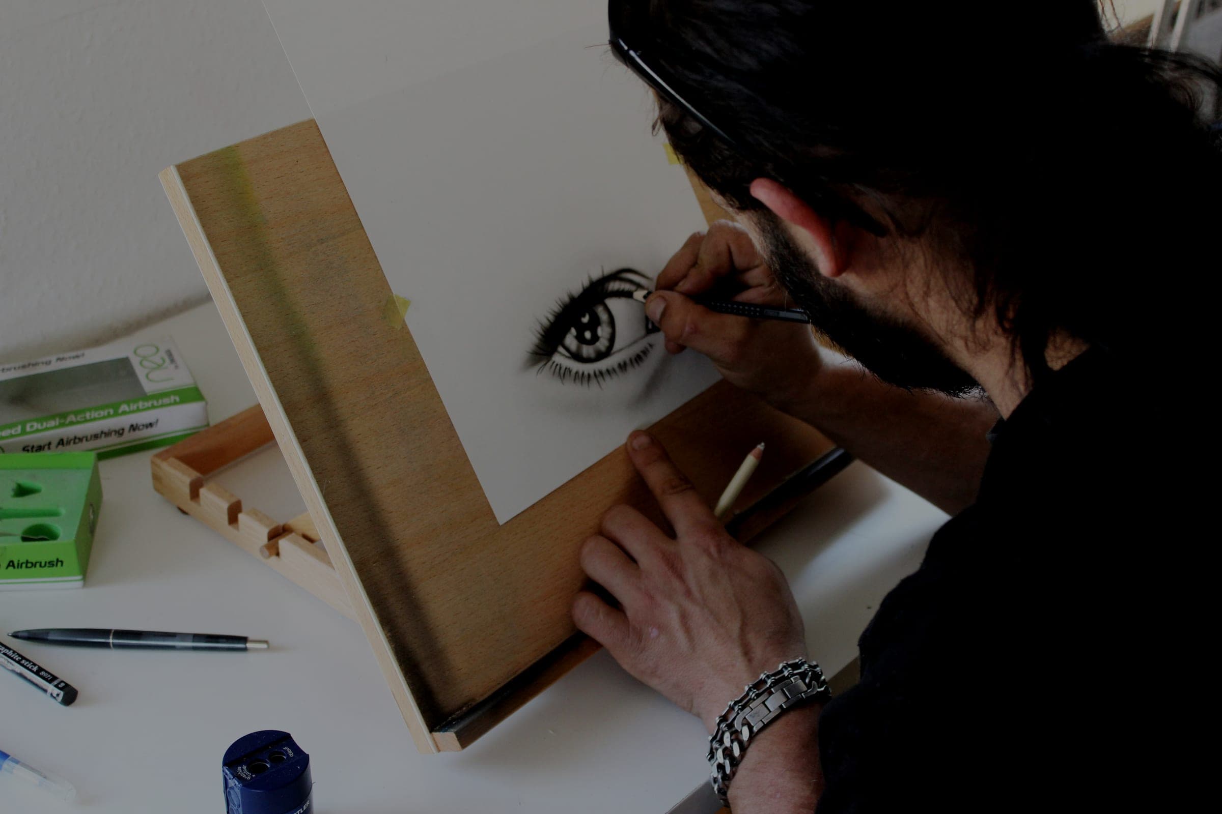 A man at a small easel drawing a detailed human eye in pencil