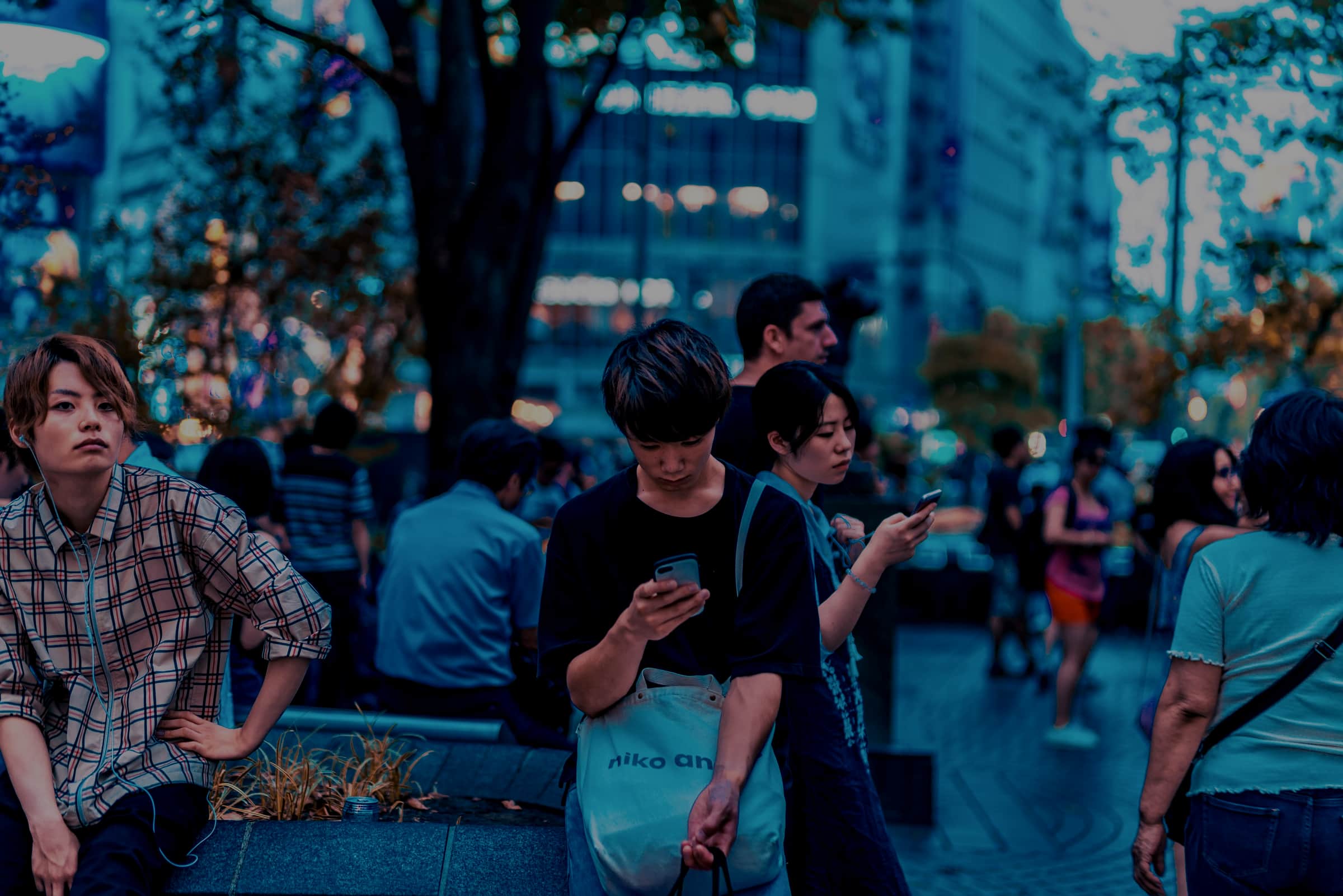 Young people standing on a city street at dusk, several looking at phones