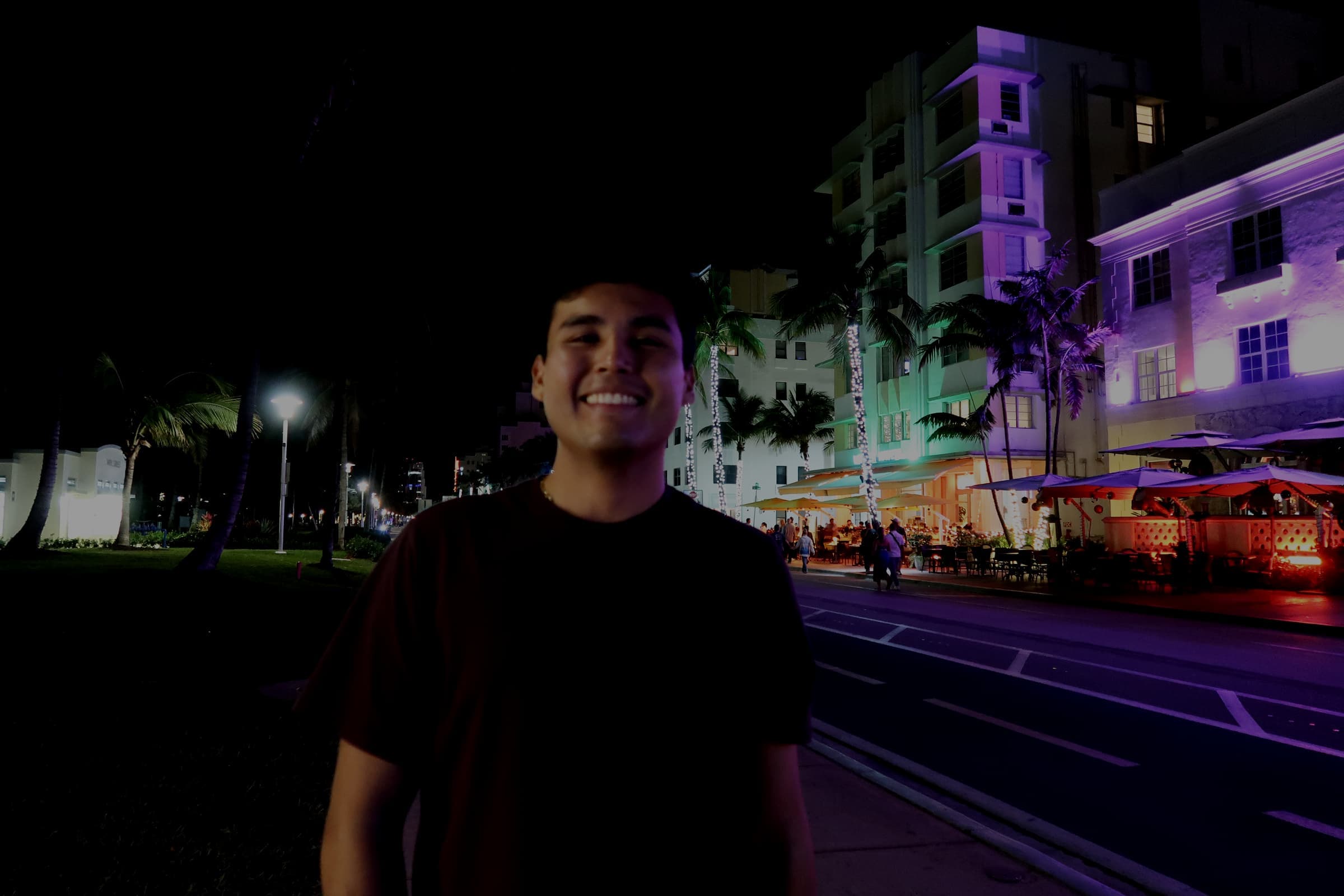 Jeffrey Escobar on Ocean Drive in Miami Beach at night, with neon-lit Art Deco hotels behind him