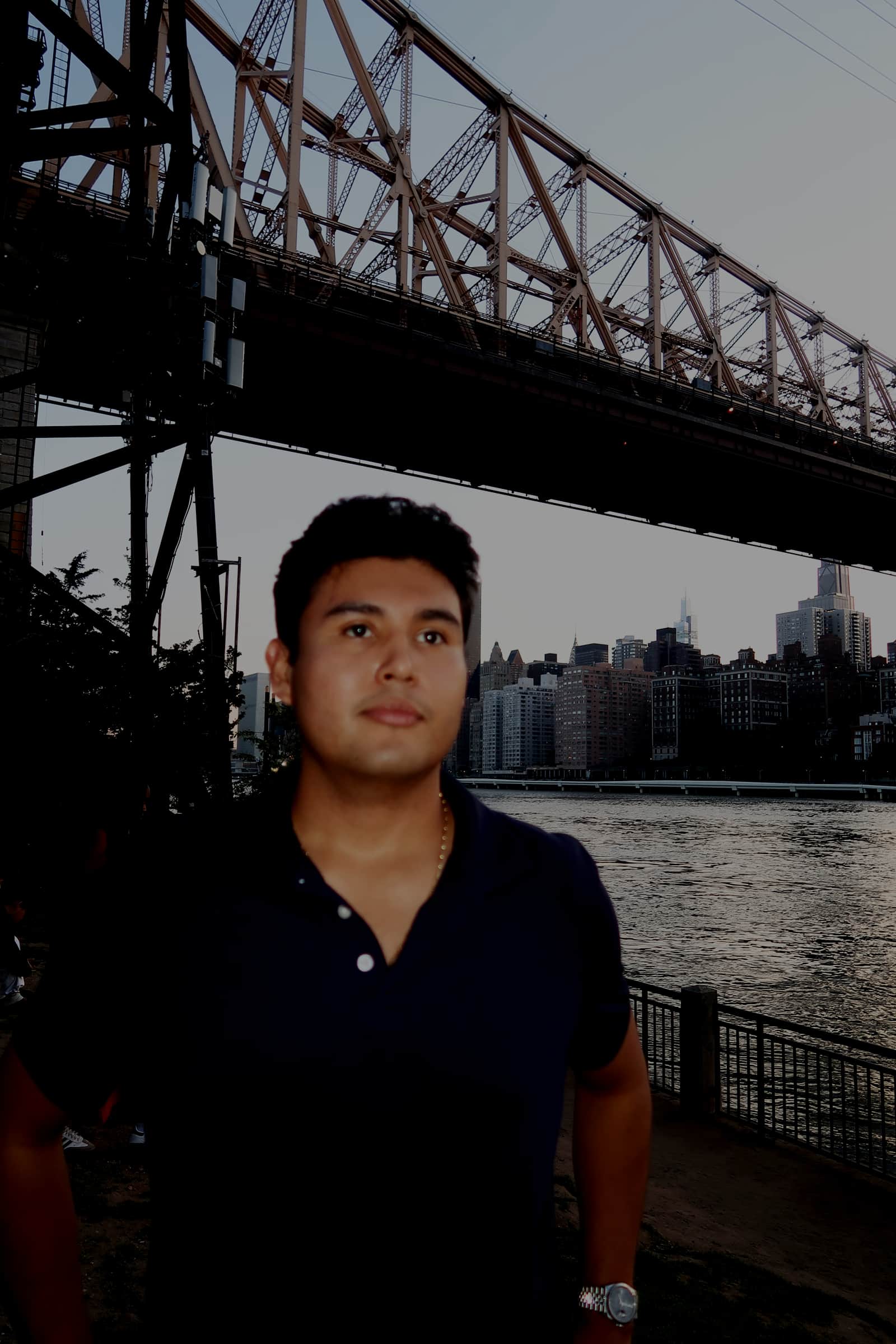Jeffrey Escobar in New York City at dusk, with the Queensboro Bridge and Manhattan skyline behind him