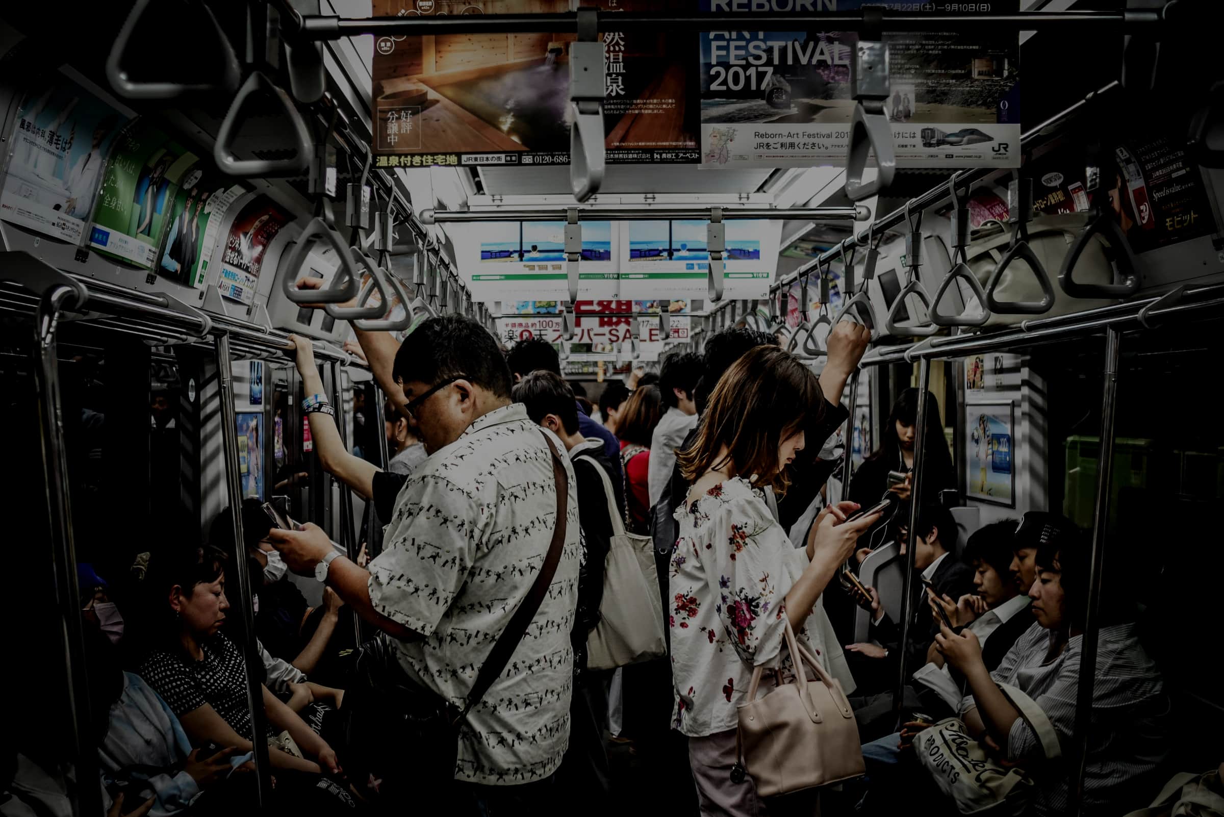 A crowded Tokyo subway car, most passengers looking down at their phones