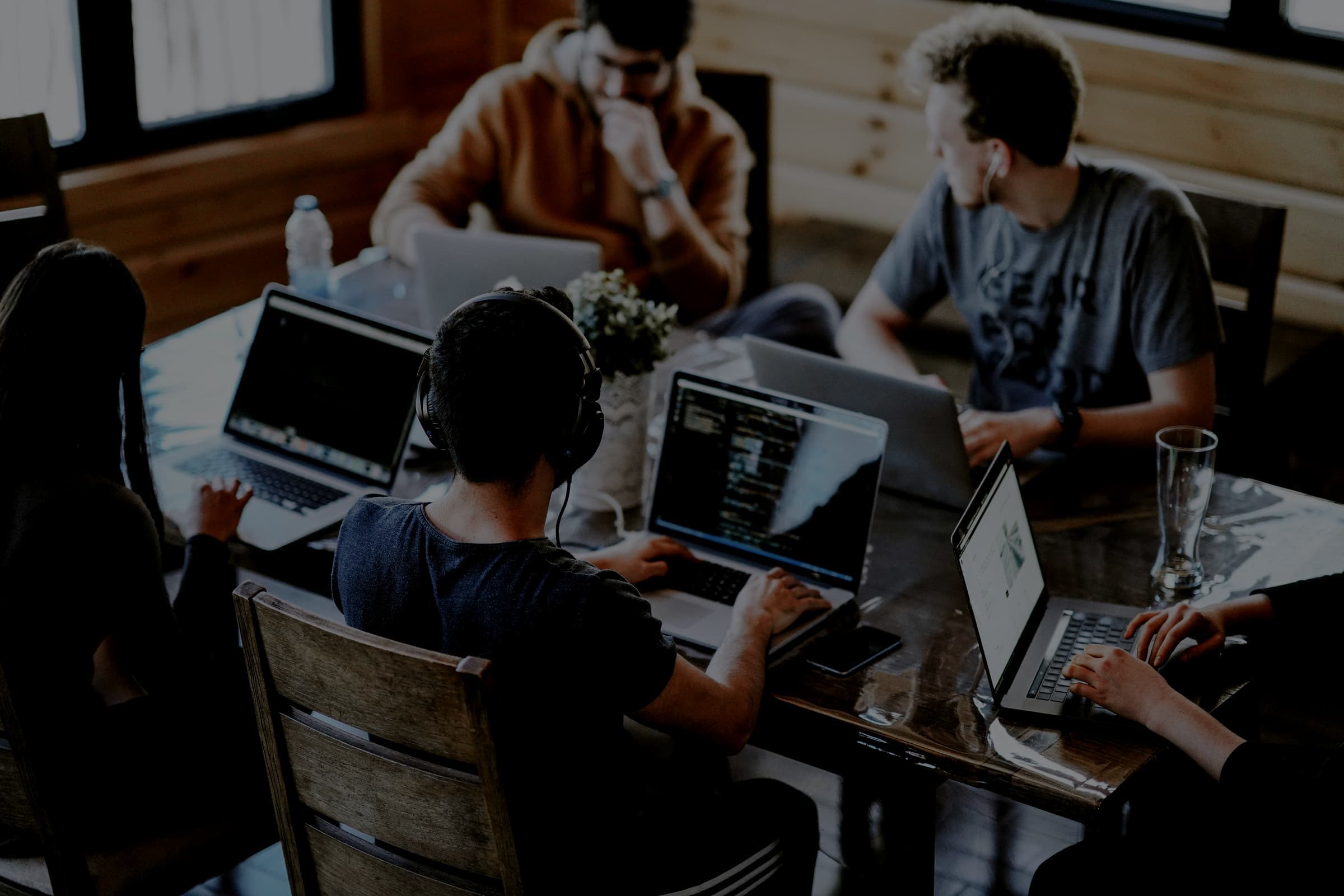 Five people working on laptops around a wooden table in a timber room