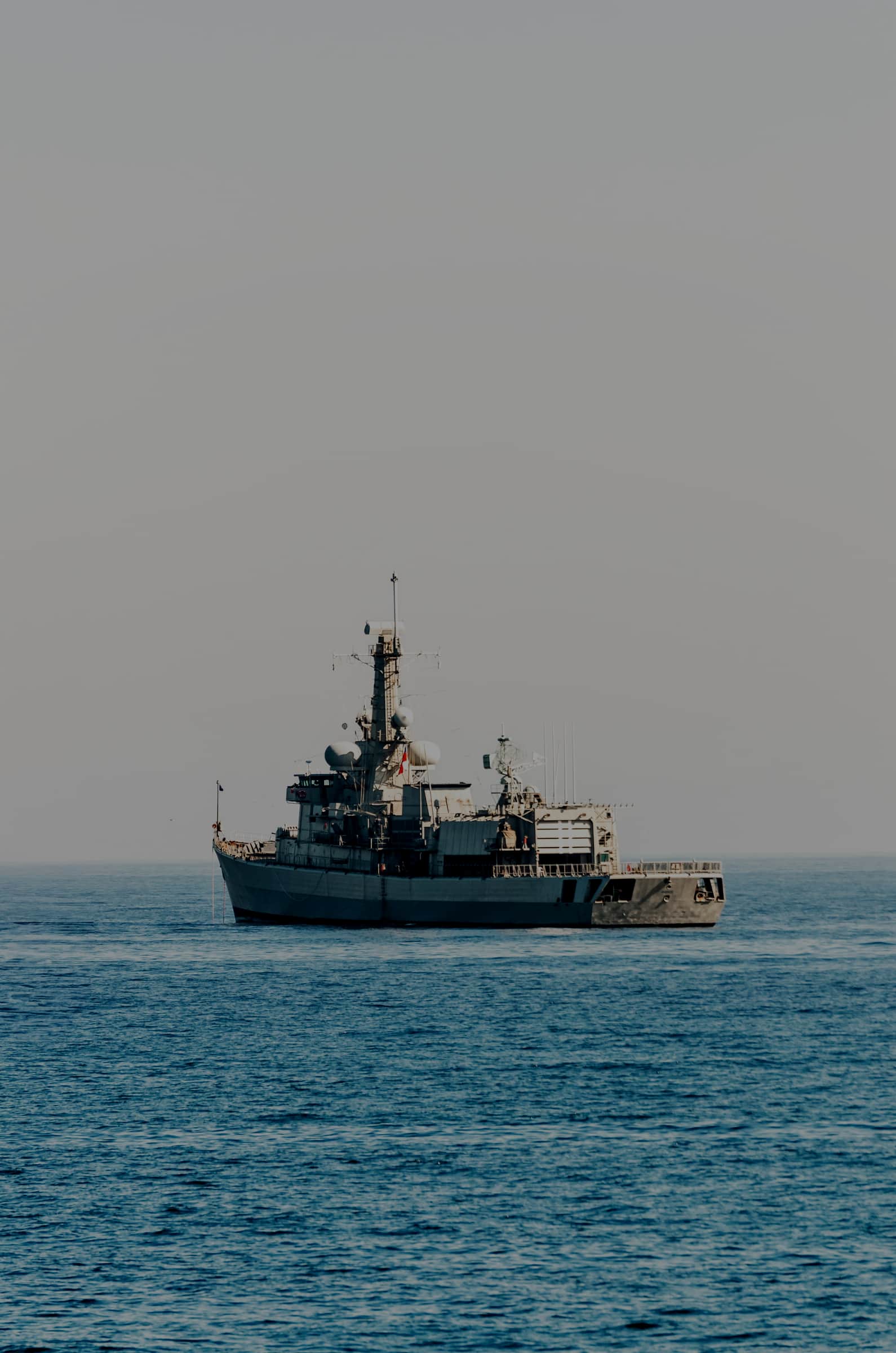 A grey naval frigate sitting alone on open blue water under a pale sky