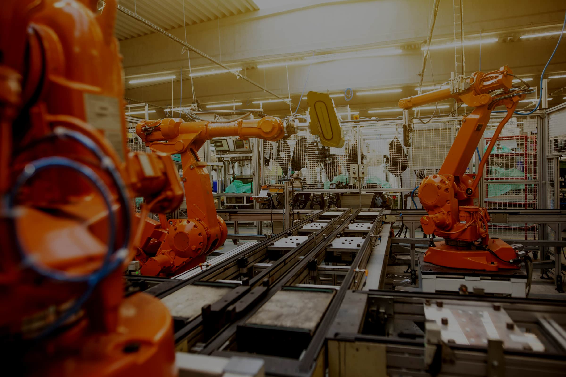 Orange industrial robot arms working over a conveyor line in a lit factory hall