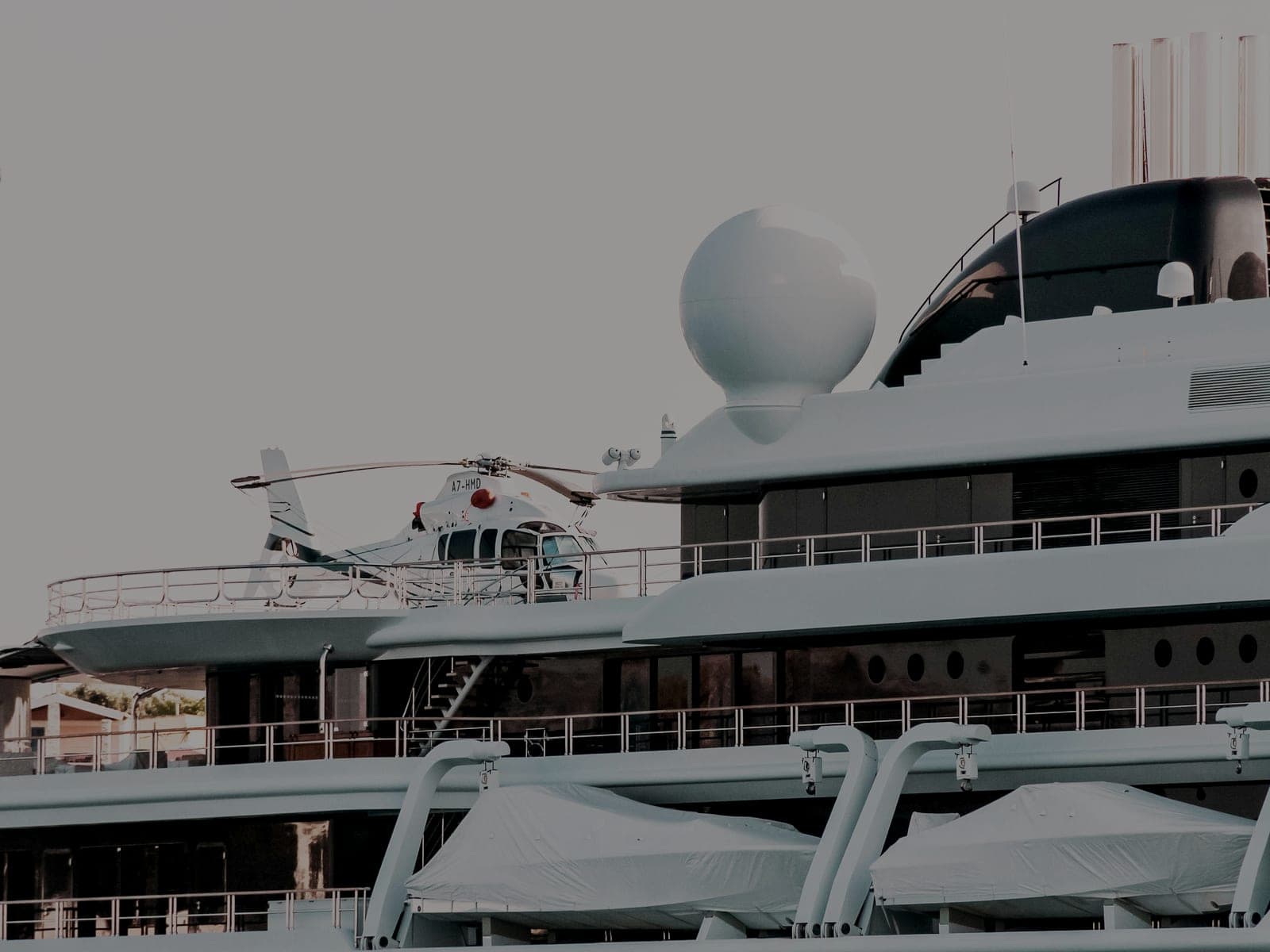 The stacked decks of a large white superyacht with a helicopter parked on the helipad
