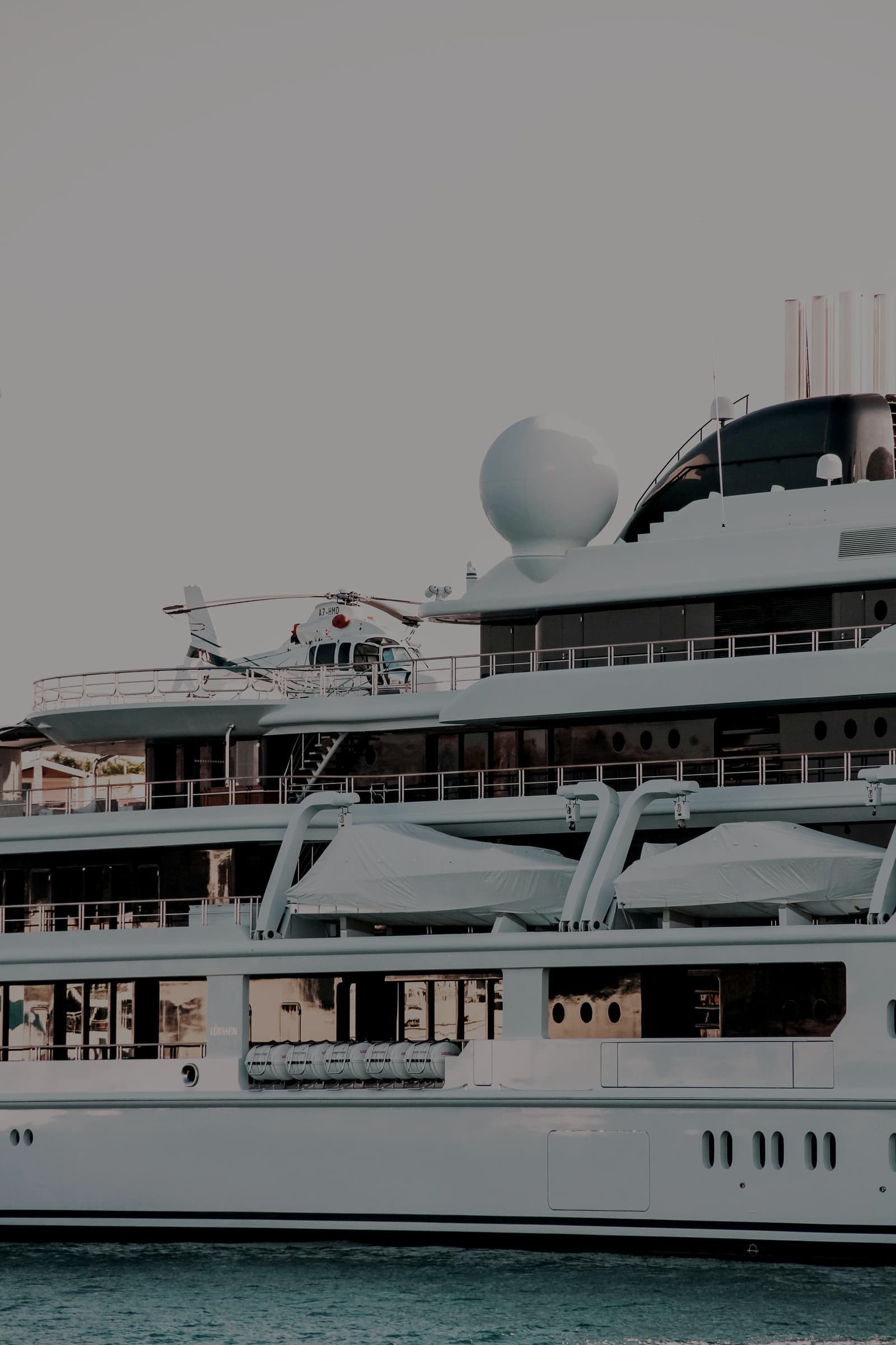 The stacked decks of a large white superyacht with a helicopter parked on the helipad