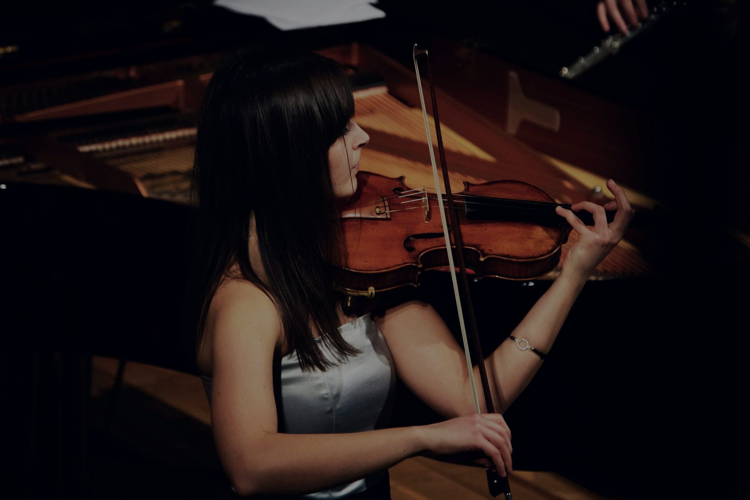 A violinist performing beside an open grand piano