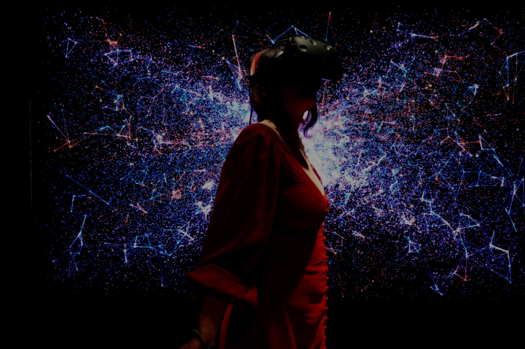 A woman in a red dress wearing a VR headset, standing in front of a wall of blue and pink particle light