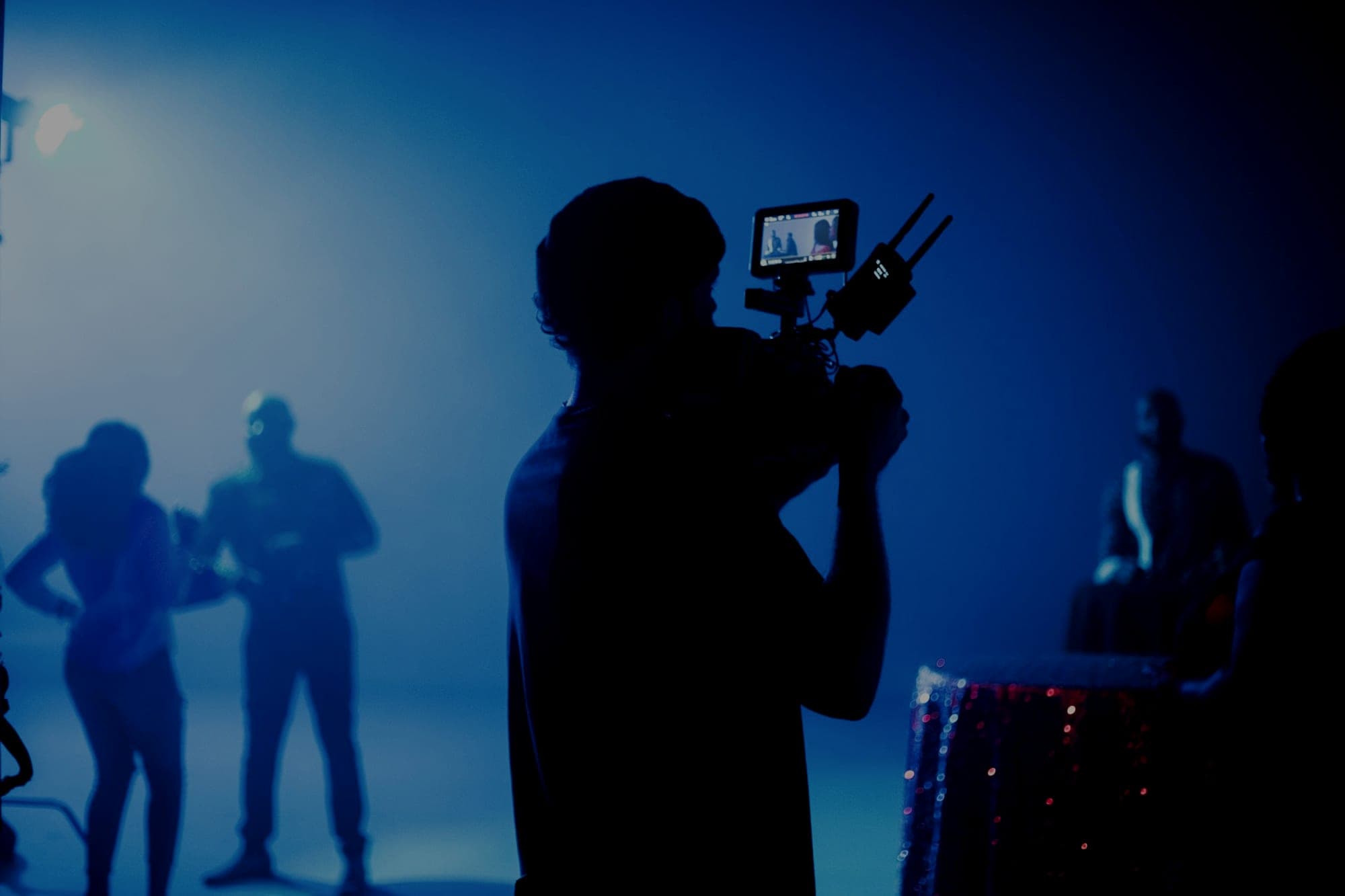 The silhouette of a camera operator filming a scene on a smoke-filled set washed in blue light
